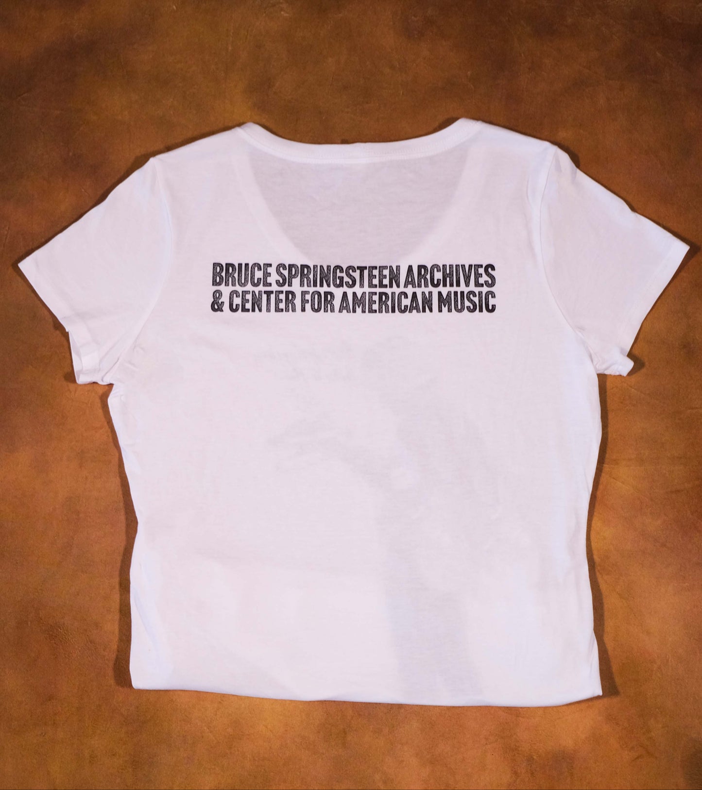 White t-shirt with Bruce Springsteen Archives and Center for American Music Logo on a brown surface