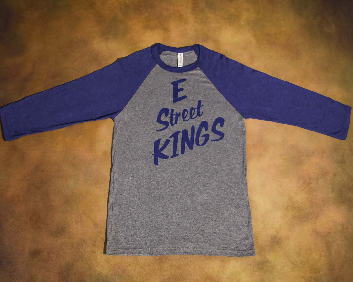 Gray and blue long-sleeve shirt with 'E Street Kings' text on a brown surface