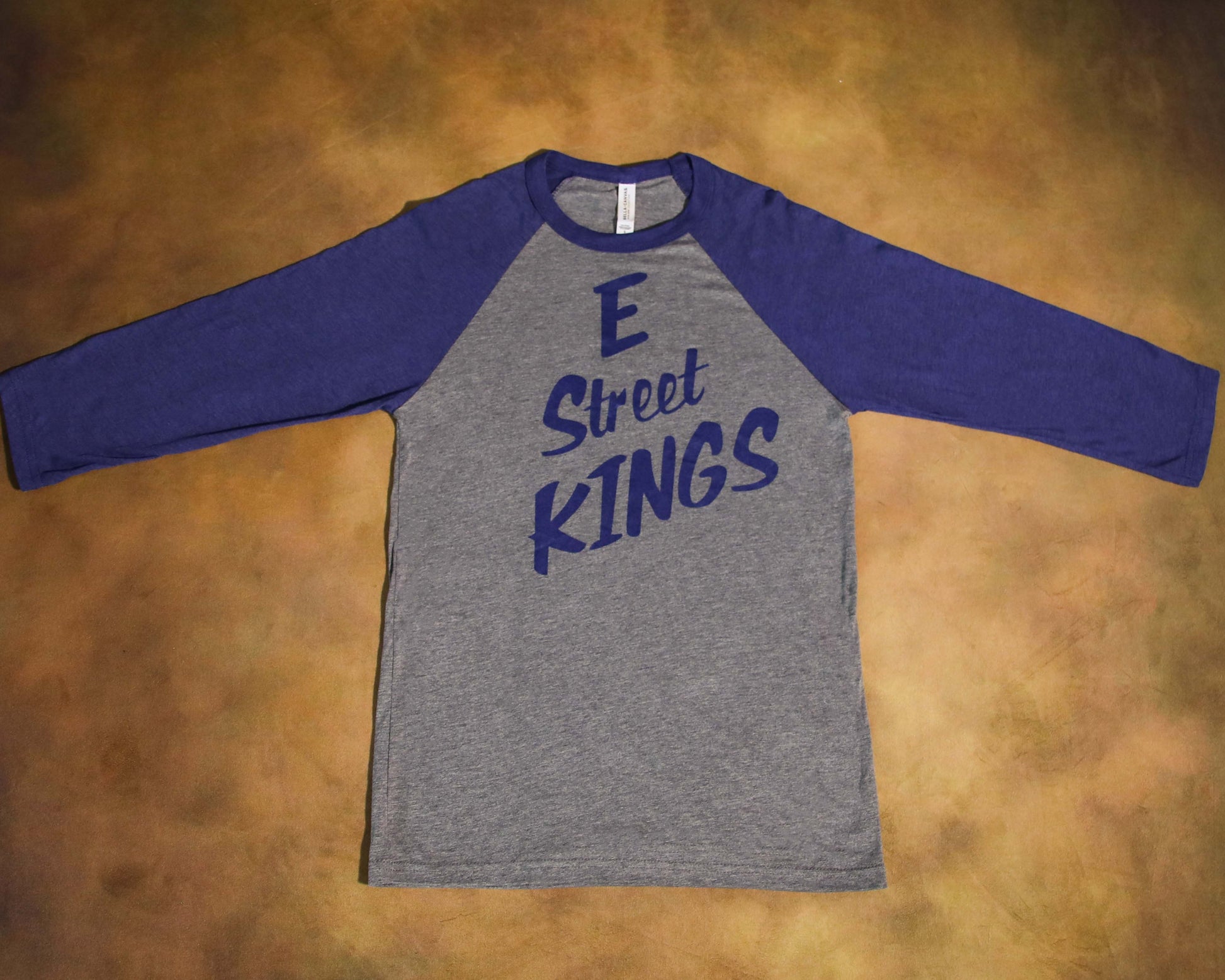 Gray and blue long-sleeve shirt with 'E Street Kings' text on a brown surface