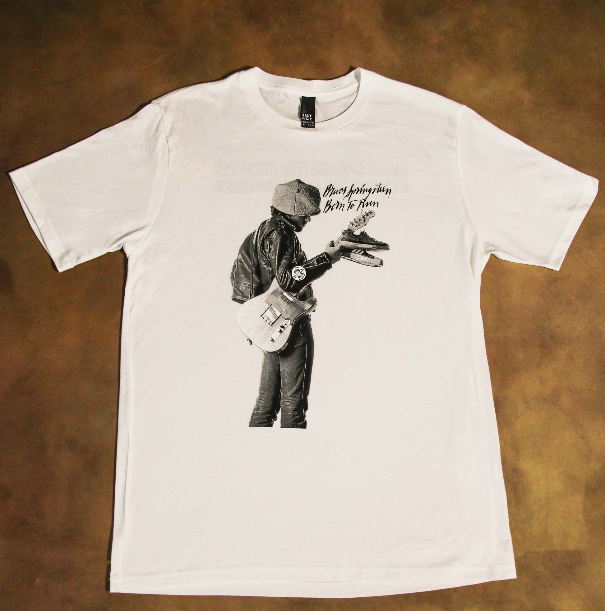 White t-shirt with Bruce Springsteen and a guitar with shoes hanging off on a brown background